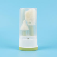 A set of three silicone baby cleaning brushes inside a clear cylindrical storage case with a white base and light green bottom, set against a solid light blue background.