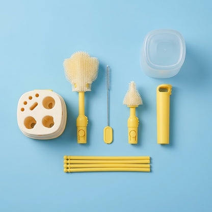 A baby bottle cleaning set arranged on a light blue background, including a clear plastic bottle lid, a beige silicone bottle brush, a yellow bottle brush, a metal cleaning brush, a yellow bottle opener, a beige silicone holder, and several yellow straw-like pieces.