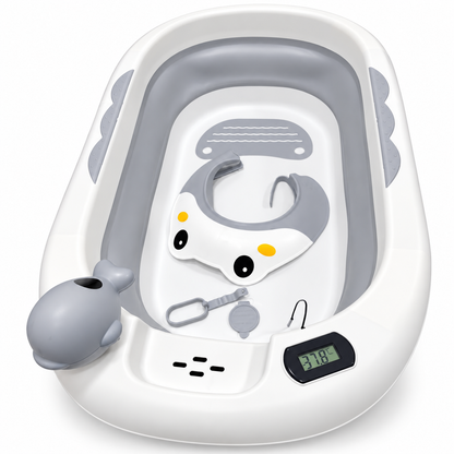 A baby bath tub set with a white exterior, gray interior, and included accessories including a whale-shaped handheld shower attachment, a small digital thermometer, and a gray and white baby head support seat with cartoon eyes.